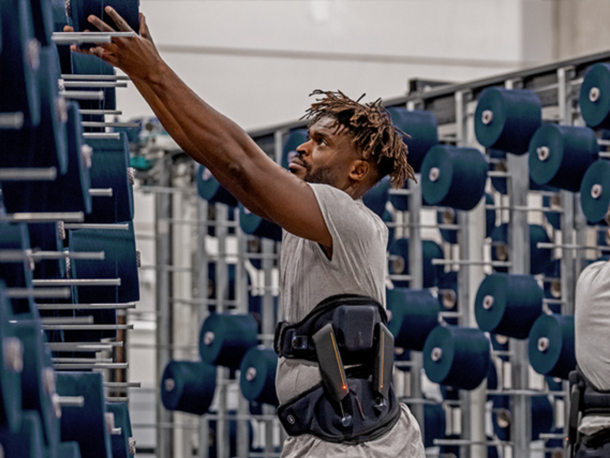 A man wearing an exoskeleton for back protection is working in a production facility.