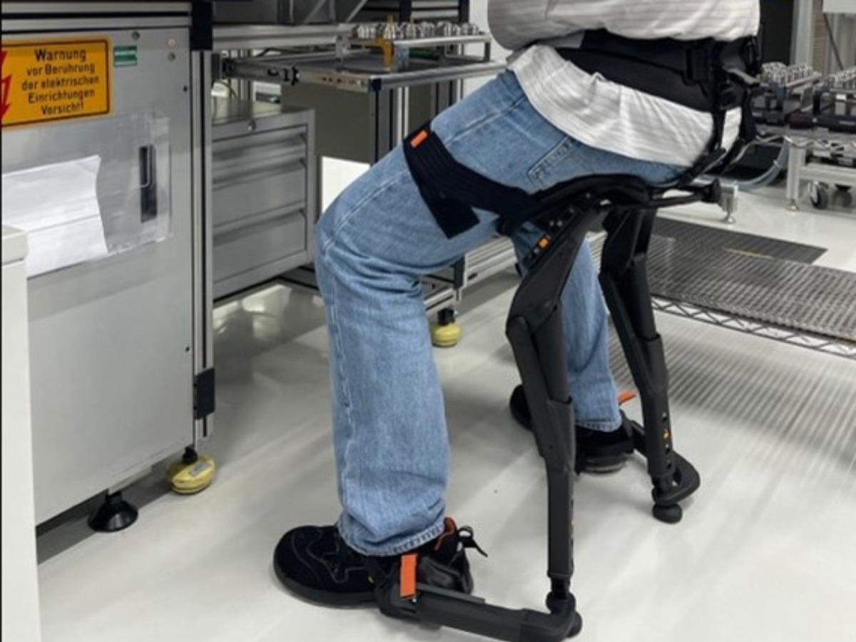 A man sitting on a Chairless Chair exoskeleton while working at a CNC machine.