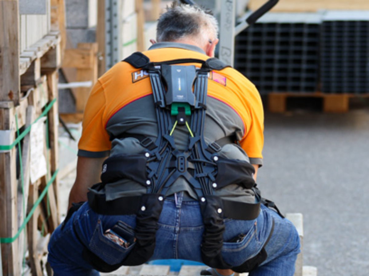 A large man wearing an exoskeleton for back protection while lifting heavy materials.